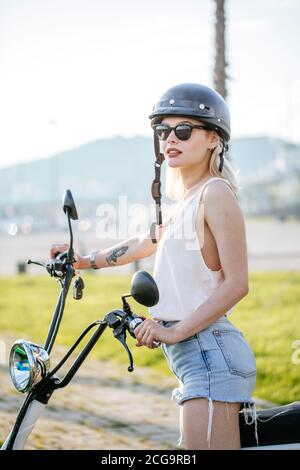 Gesunde Lebensweise - junge hübsche Mädchen oder Frau in Helm Erholung mit Motorrad oder Elektrofahrrad im tropischen Palmengarten Oder Gasse Stockfoto