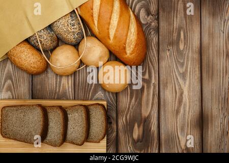 Brot und Brötchen in einer Papiertüte auf einem hölzernen Hintergrund, in Scheiben geschnittene Stücke von schwarzem Brot Stockfoto