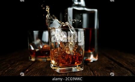 Spritzt Whiskey aus Glas mit Eiswürfeln innen. Bewegung einfrieren von Stockfoto