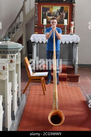 28. August 2020, Sachsen, Kossa: Nach dem Glockengeläut der kleinen Kirche in Kossa kann der 18-jährige Janus Deutrich den renovierten Kirchenraum für Proben mit seinem Alphorn nutzen. Der Lehrling Förster, der seit seinem 10. Lebensjahr neben Trompete und Jagdhorn das Alphorn spielt, freut sich über den ungewöhnlichen Proberaum. Seit einem halben Jahr läutet er täglich die Glocken der Kirche von Hand, um "am Ende des Tages zu läuten". Pastor Andreas Ohle freut sich über den Musikliebhaber, der nach einigen Jahren des Schweigens wieder die Glocken läuten lässt und die Litte benutzt Stockfoto