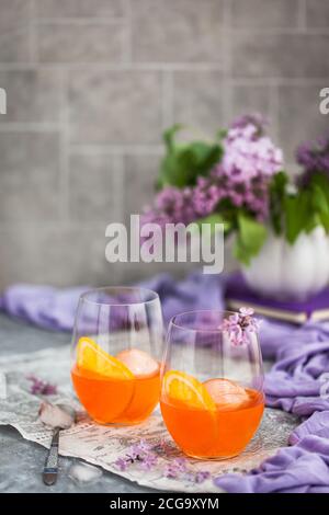 Orange Aperol Spritz Cocktail in einem Weinglas serviert, dekoriert mit einer Scheibe Orange und Flieder Stockfoto