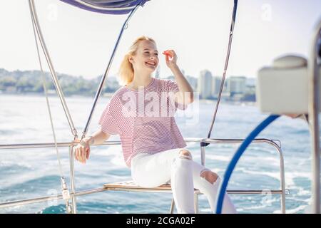 Blonde attraktive Frau auf weißer Yacht in einem nautischen Thema. Blonde Haare, gestreifte Bluse. Sommer-Outfit für Schifffahrt im offenen Meer oder Meer Stockfoto