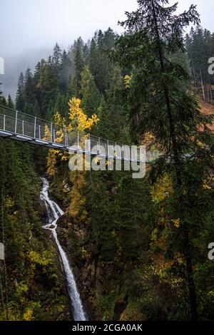 Hängebrücke aus Metall über dem schönen Rabby-Tal im Nebel irgendwo in Norditalien im Frühherbst. Stockfoto