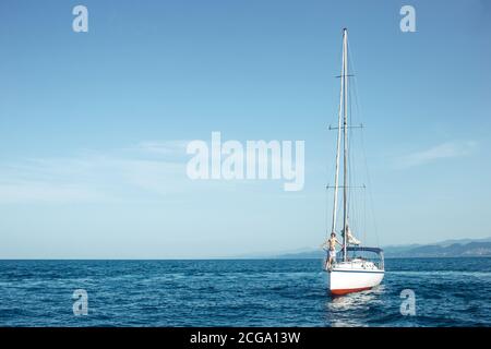 Schwimmende Yacht mit Segeln hinunter in ruhiger See. Ein Boot senkte die Segel und ankerte nahe der Küste Stockfoto