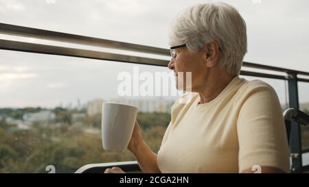 Ältere Frau im Rollstuhl auf der Terrasse mit einer Tasse Tee oder Kaffee. . Hochwertige Fotos Stockfoto
