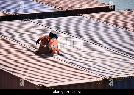 Stevedore mit weißem Helm und hoher Sichtbarkeit orange Weste, die eine Pause auf der Oberseite der Container während der Ladung Betrieb der Be-und Entladung. Stockfoto