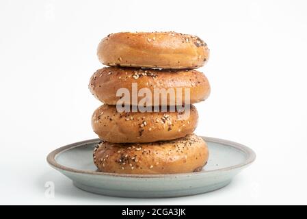 Ein einzelner großer Stapel von vier frisch gebackenen Bagels auf einem Keramikplatte auf einem schlichten weißen Hintergrund. Stockfoto