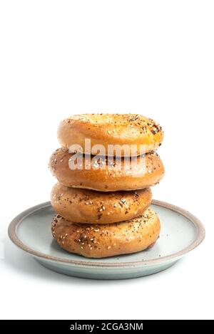 Ein einzelner großer Stapel von vier frisch gebackenen Bagels auf einem Keramikplatte auf einem schlichten weißen Hintergrund. Stockfoto