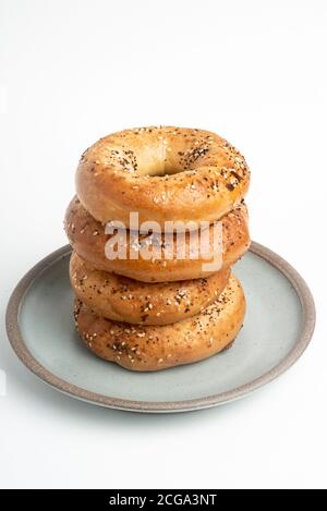 Ein einzelner großer Stapel von vier frisch gebackenen Bagels auf einem Keramikplatte auf einem schlichten weißen Hintergrund. Stockfoto