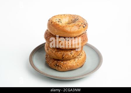 Ein einzelner großer Stapel von vier frisch gebackenen Bagels auf einem Keramikplatte auf einem schlichten weißen Hintergrund. Stockfoto