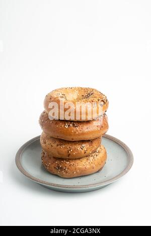 Ein einzelner großer Stapel von vier frisch gebackenen Bagels auf einem Keramikplatte auf einem schlichten weißen Hintergrund. Stockfoto