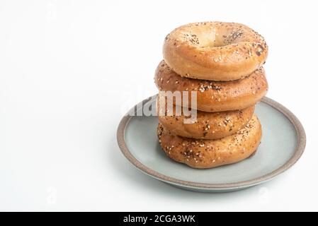 Ein einzelner großer Stapel von vier frisch gebackenen Bagels auf einem Keramikplatte auf einem schlichten weißen Hintergrund. Stockfoto