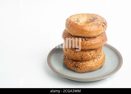 Ein einzelner großer Stapel von vier frisch gebackenen Bagels auf einem Keramikplatte auf einem schlichten weißen Hintergrund. Stockfoto