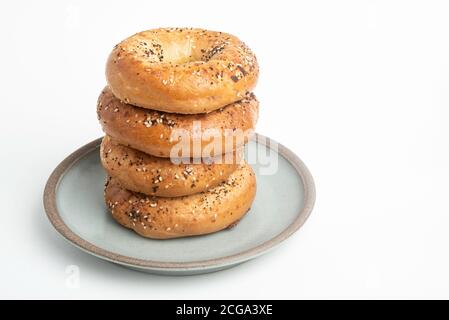 Ein einzelner großer Stapel von vier frisch gebackenen Bagels auf einem Keramikplatte auf einem schlichten weißen Hintergrund. Stockfoto