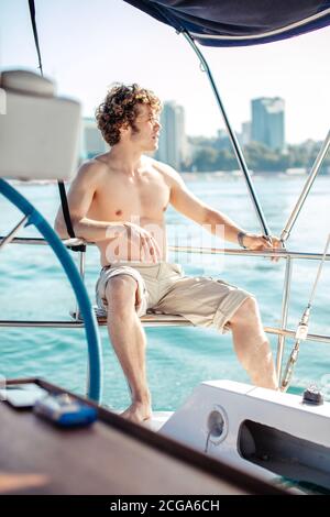 Junge Red-Head Hipster Mann mit krausem Haar sitzt ohne Hemd, glücklich entspannen auf dem Urlaub Segelboot Yacht mit einer Pause auf Sommerboot über b Stockfoto