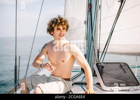 Junge Rotkopfmann mit krausem Haar entspannend glücklich auf der Urlaub Segelboot Yacht mit einer Pause auf Sommerboot über Blauer Ozean Welle Hintergrund Stockfoto