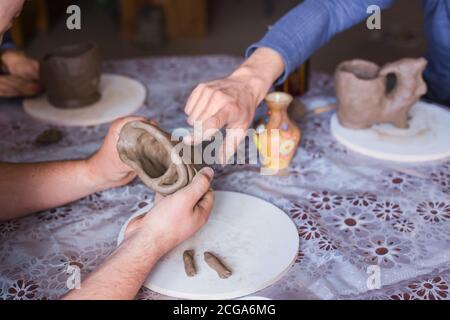 Töpferklasse und Werkstatt: Professioneller männlicher Töpfer zeigt, wie man Tonkrug in Töpferei macht - Nahaufnahme. Handgemacht, Kunst und Studienkonzept Stockfoto