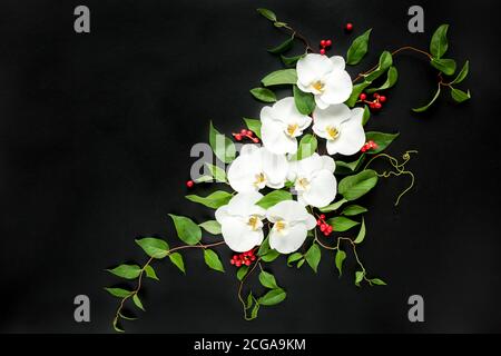 Komposition aus weißen Orchideen und grünen Blättern auf schwarzem Hintergrund. Flach liegend, Draufsicht. Rahmen aus Blumen. Blumenmuster. Stockfoto
