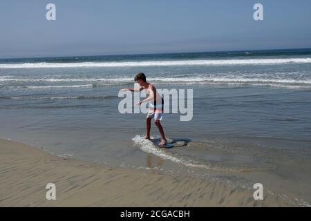 Ein Teenager geht Skim Boarding auf den Wellen am nächsten an der Strandküste. Stockfoto