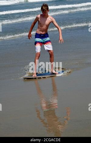 Ein Teenager geht Skim Boarding auf den Wellen am nächsten an der Strandküste. Stockfoto