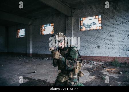 Soldat in voller US MARSOC bewaffnet mit Sturmgewehr durch das verlassene Gebäude laufen. Militärischer Zusammenstoß. Stockfoto