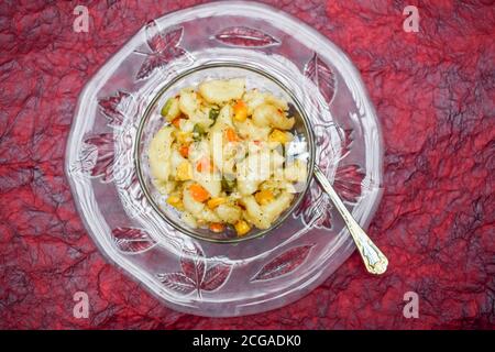 Nahaufnahme von Gemüse Makkaroni in weißer Sauce in einer transparenten Schüssel auf weißem Hintergrund isoliert gekocht serviert. Gekochte Pasta mit Karotten, Mais, Kapsik Stockfoto