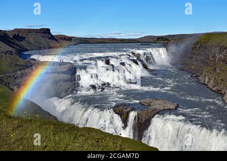 Ein Regenbogen erscheint über Gullfoss. Alle drei Stufen des Wasserfalls werden gesehen, wie sie aus der Sicht in einen Canyon fallen. Golden Circle, Südwestisland. Stockfoto