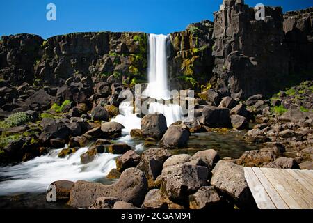 Oxararfoss, wie es an einem klaren sonnigen Tag über Felsbrocken kaskadiert. Die Promenade für Besucher ist sichtbar. Thingvellir Nationalpark, Goldener Kreis, Island Stockfoto