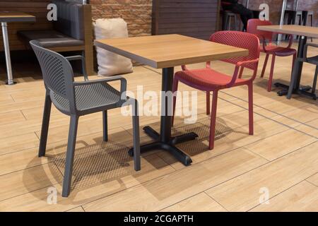 Kleiner Tisch aus Holz und Metall mit zwei Stühlen, einer rot und der andere grau, mit einem Holzboden, im Hintergrund befinden sich weitere Tische, Stühle und ein Stockfoto