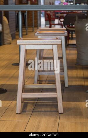 Nahaufnahme von Holzbänken und schwimmenden Boden, im Hintergrund andere kleine Holzbank in einem Restaurant an einem sonnigen Morgen Stockfoto