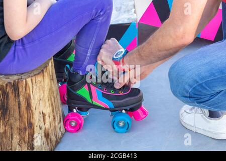 Nahaufnahme eines Vaters, der Rollschuhe auf seine Tochter legt, man kann ihre Gesichter nicht sehen Stockfoto