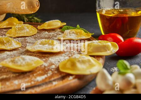 Leckere Ravioli mit Mehl, Kirschtomaten, Sonnenblumenöl und Basilikum auf dunklem Grund. Der Prozess der Herstellung von italienischen Ravioli. Seitenansicht. Stockfoto