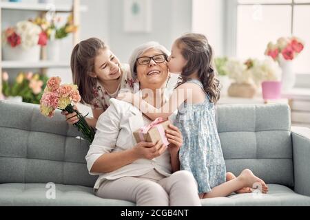 Alles gute zum Muttertag! Kinder Töchter gratulieren Oma geben ihr Blumen und Geschenk. Oma und Mädchen lächeln und umarmen. Familienurlaub und Stockfoto