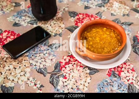 Locro, typisch argentinische und traditionelle Gerichte auf handgemachtenem Ton, begleitet von Brot und einem Glas Wein, mit Löffeln. Stockfoto