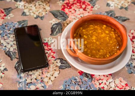 Locro, typisch argentinische und traditionelle Gerichte auf handgemachtenem Ton, begleitet von Brot und einem Glas Wein, mit Löffeln. Stockfoto