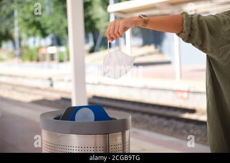 Unkenntlich junge Frau, die gebrauchte schmutzige chirurgische Maske in einen Mülleimer. Coronavirus-Konzept. Stockfoto