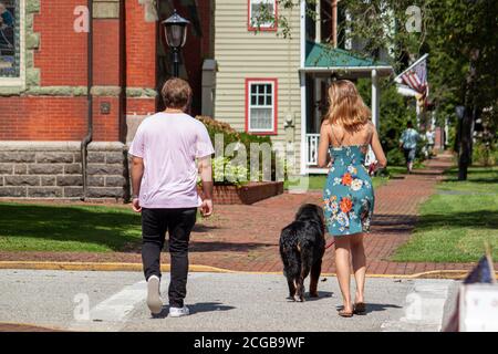 Ein junges kaukasisches Paar geht mit ihrem Hund durch den historischen Bezirk Chestertown, Maryland. Die Frau hat helle Haarfarbe und trägt florale Stockfoto