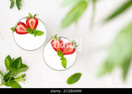 Gesunder Erdbeerjoghurt mit in Gläsern mit frischen Beeren über weißem Tisch. Draufsicht durch Blätter der Minze mit Kopierraum Stockfoto