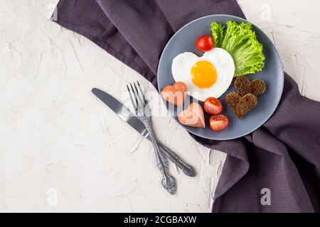 Valentinstag Frühstück mit herzförmigen Spiegeleier serviert auf grauen Teller. Flat Lay, Draufsicht Stockfoto