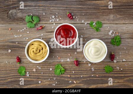 Set aus verschiedenen Saucen mit Gewürzen auf natürlichem Holzhintergrund. Mayonnaise Ketchup Senf. Draufsicht mit Kopierraum Stockfoto