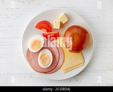 Frühstücksteller mit Käse und Schinkenwurst auf weißem Holztisch, Blick von oben Stockfoto