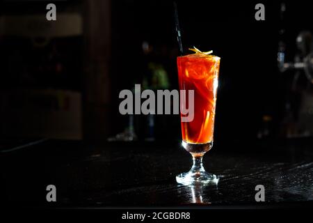 Ein roter Cocktail in einem hohen Glas steht auf der Theke einer dunklen Bar. Stockfoto