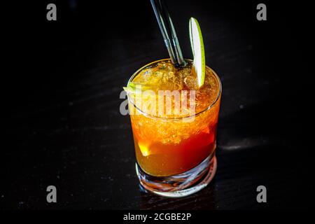 Ein Cocktail mit Whiskey oder Cognac oder Cola in einem Longdrinkglas befindet sich auf der Theke einer dunklen Bar. Stockfoto