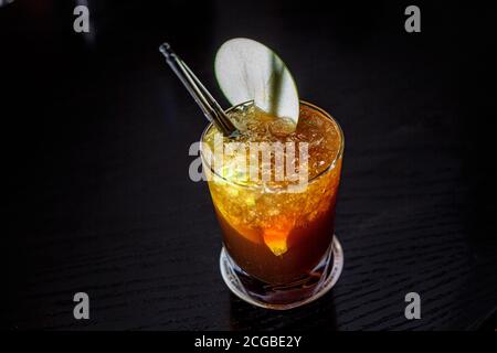 Ein Cocktail mit Whiskey oder Cognac oder Cola in einem Longdrinkglas befindet sich auf der Theke einer dunklen Bar. Stockfoto