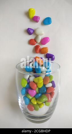 Bunte Aquarienkiesel mit Glas auf weißer Oberfläche oder Hintergrund. Stockfoto