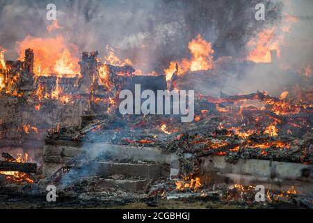 Holzhausruine mit Flammen, Glut und Rauch, nach dem Abbrennen Stockfoto