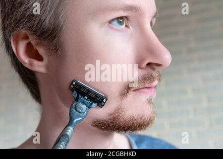 Junger Mann mit Bart und Rasierer in der Hand Nahaufnahme. Stockfoto