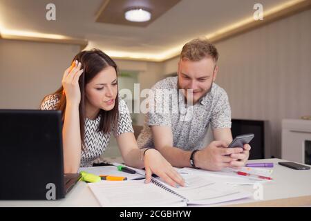 Zwei Studenten lernen zusammen, sitzen am Tisch vor Zeitungen und Laptop. Stockfoto