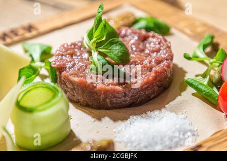 Tartare - eine traditionelle Vorspeise aus rohem Rindfleisch mit Gewürzen liegt auf einem Holzbrett im Restaurant. Stockfoto