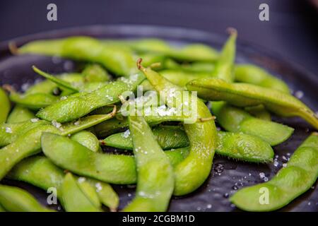 Gekochte grüne Edamame liegen auf einem dunklen Teller in einem japanischen Restaurant. Stockfoto